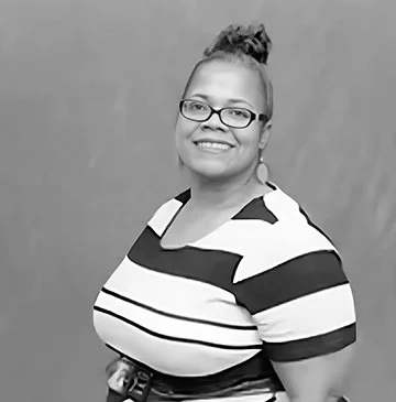 A woman with glasses and a bun hairstyle smiling, wearing a striped shirt.