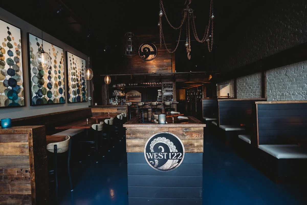 Interior of a bar or restaurant with wooden decor, seating booths, pendant lights, and artwork on the wall.