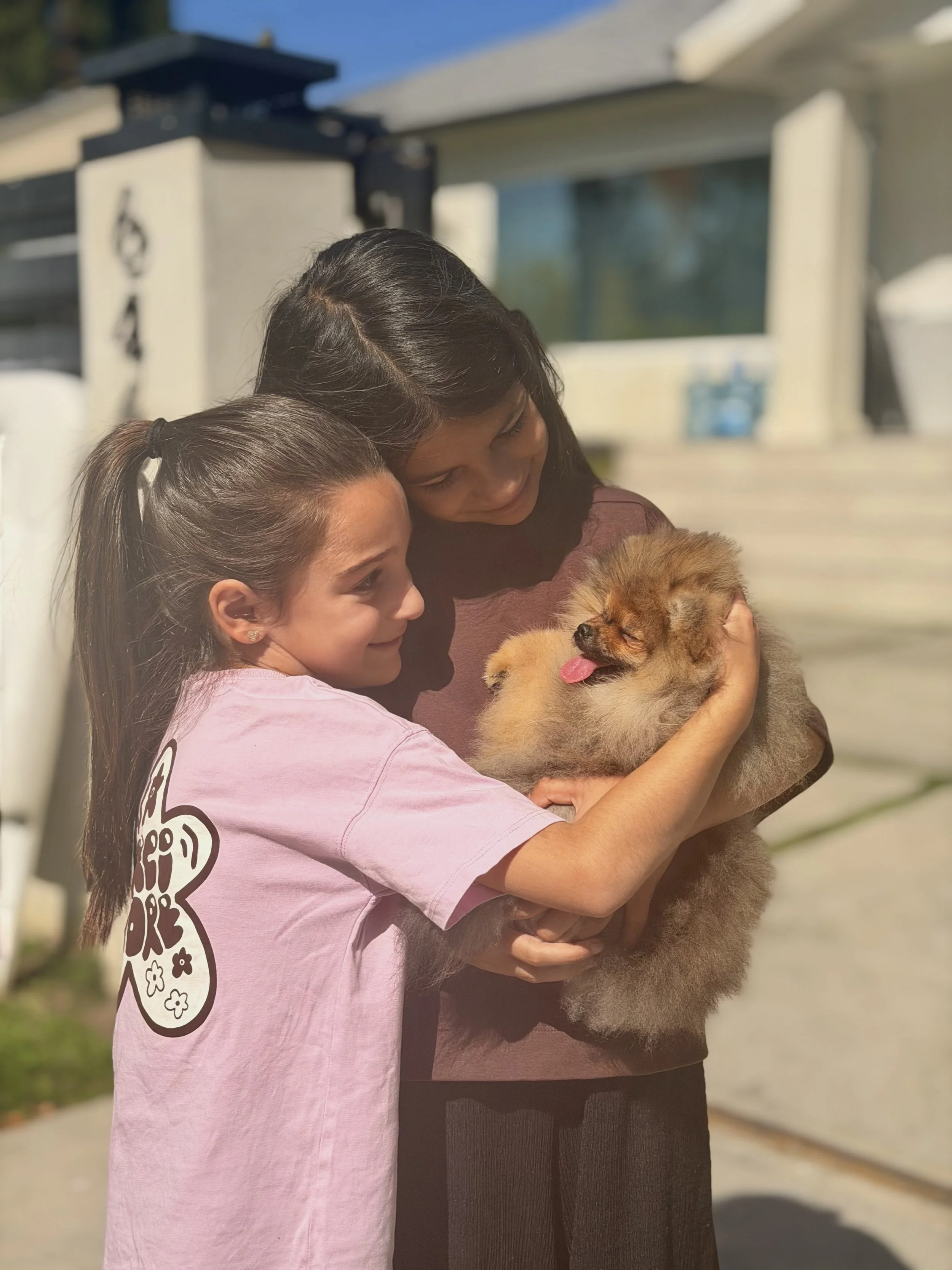 A woman and a girl holding a fluffy puppy outside on a sunny day.