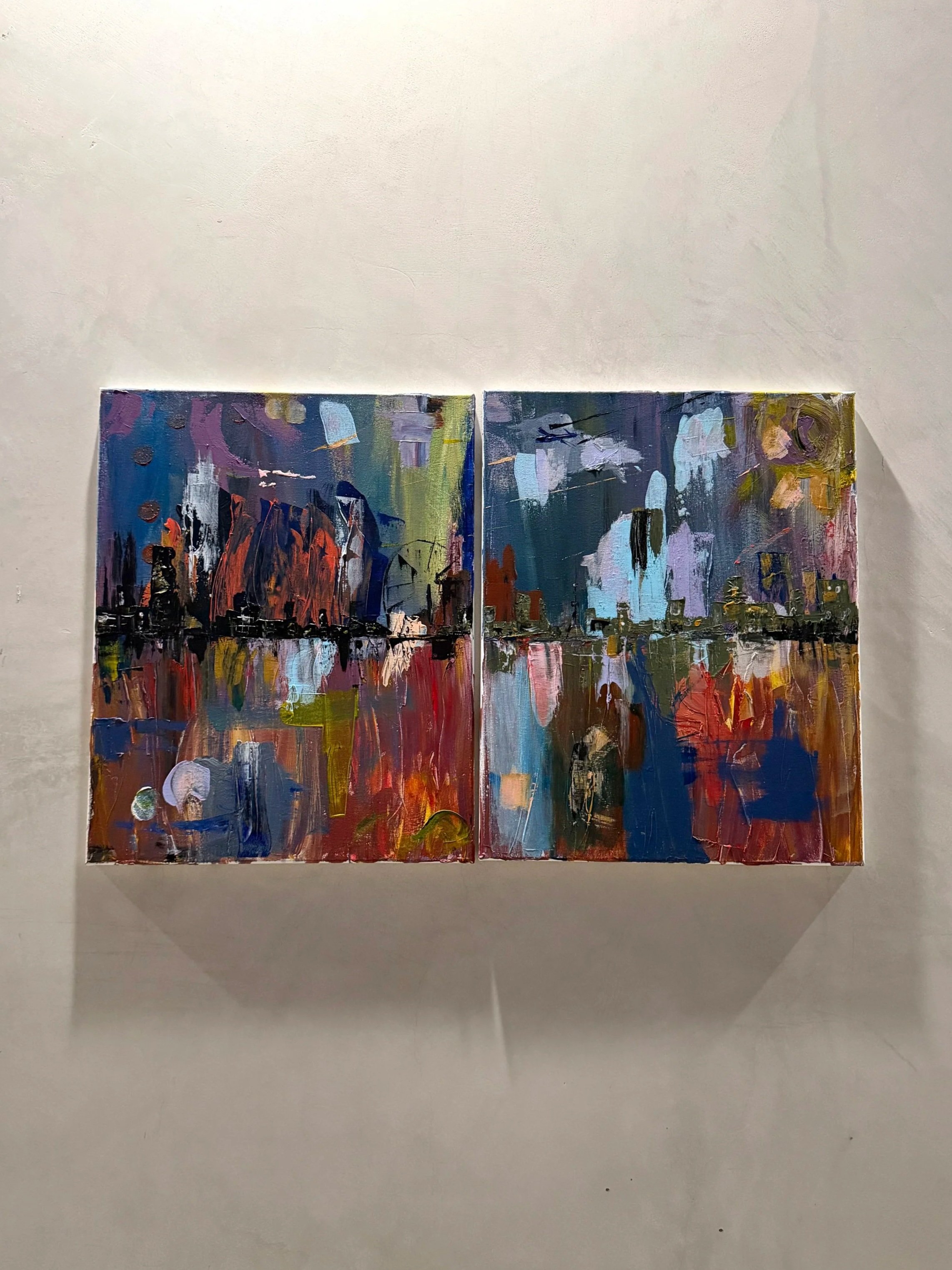 Two colorful abstract paintings hanging on a white gallery wall.