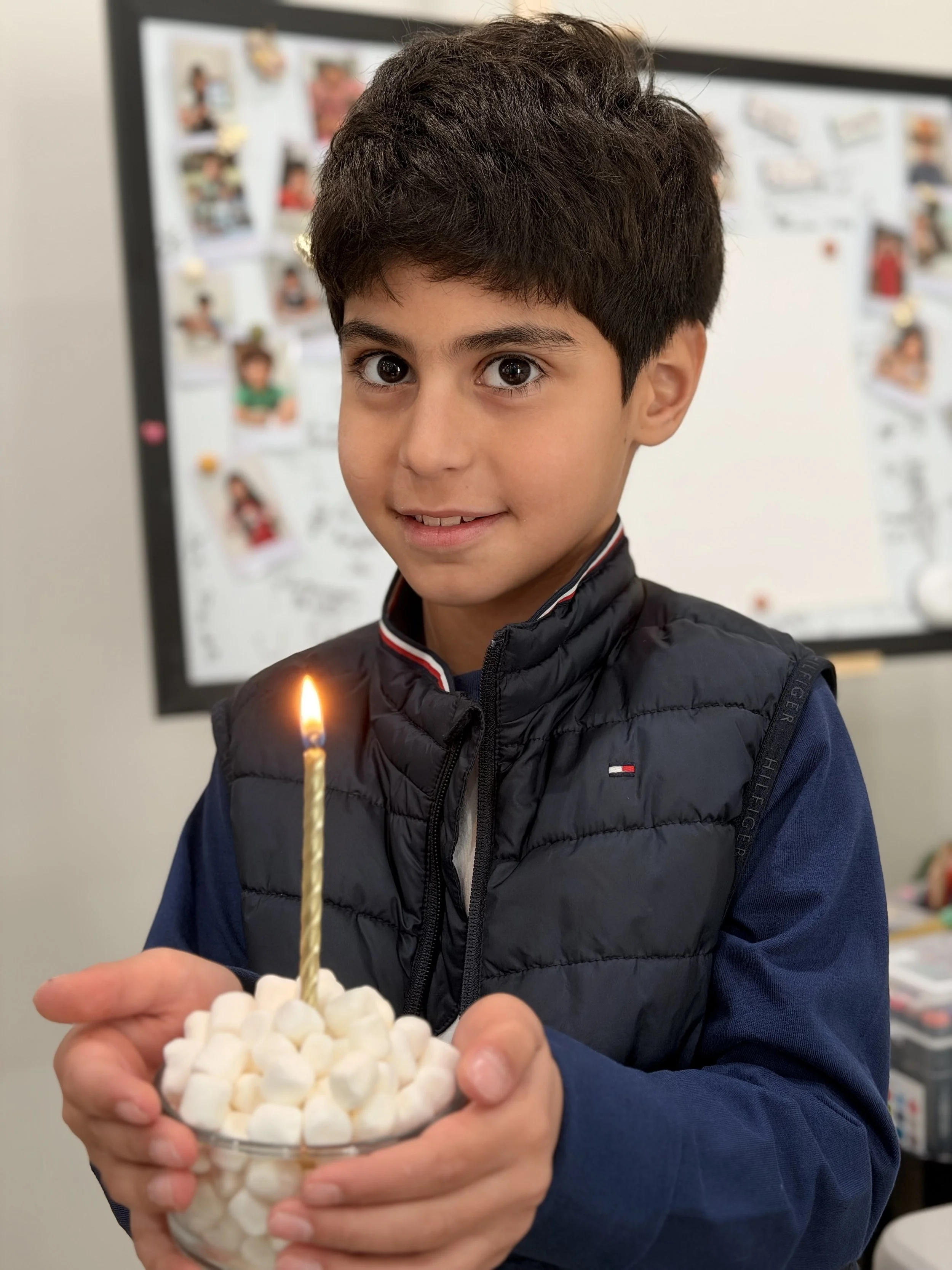 A boy holding a bowl of marshmallows with a lit birthday candle on top, celebrating a birthday.