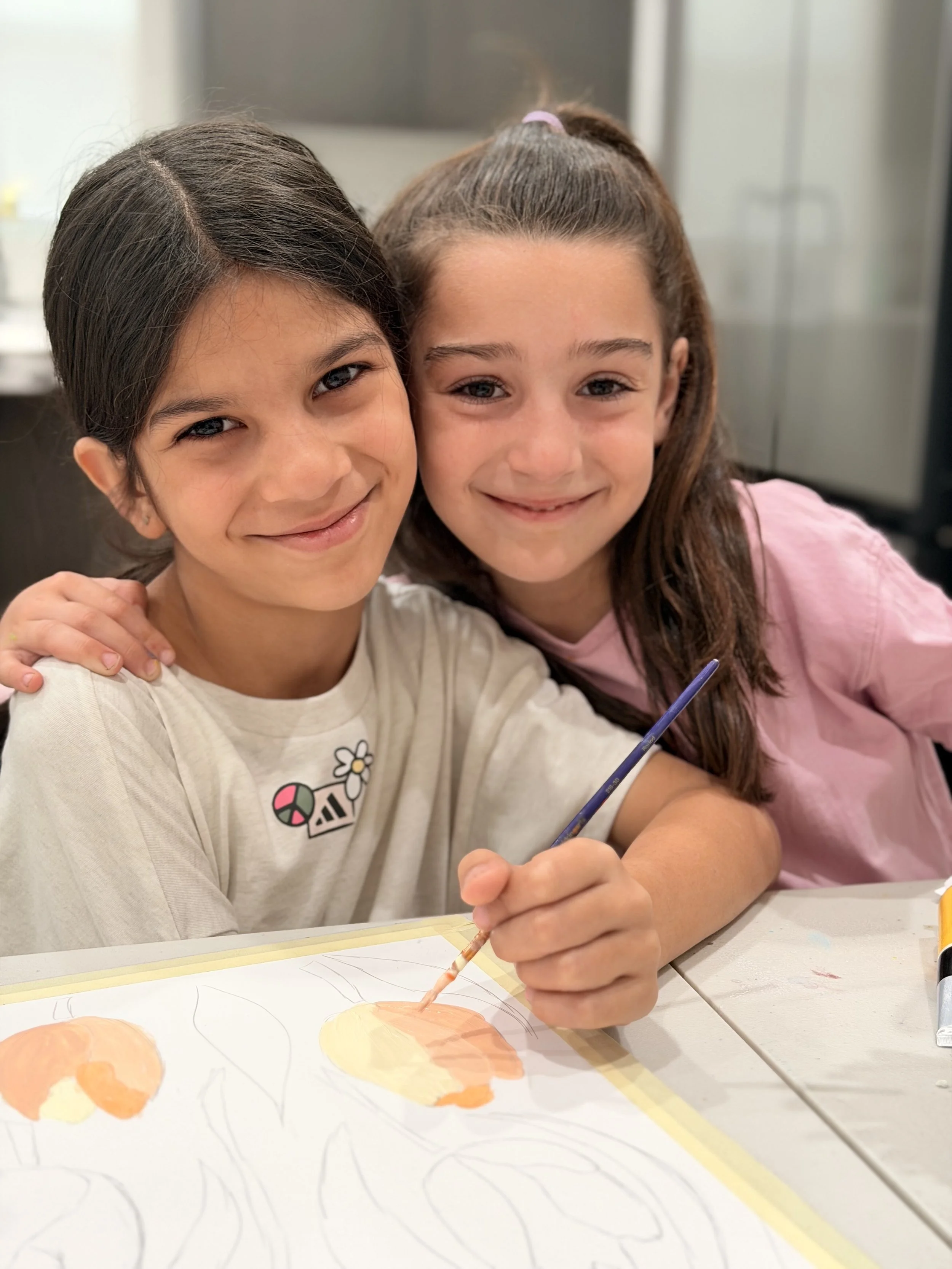 Two young girls smiling and hugging while drawing and coloring on a piece of paper.