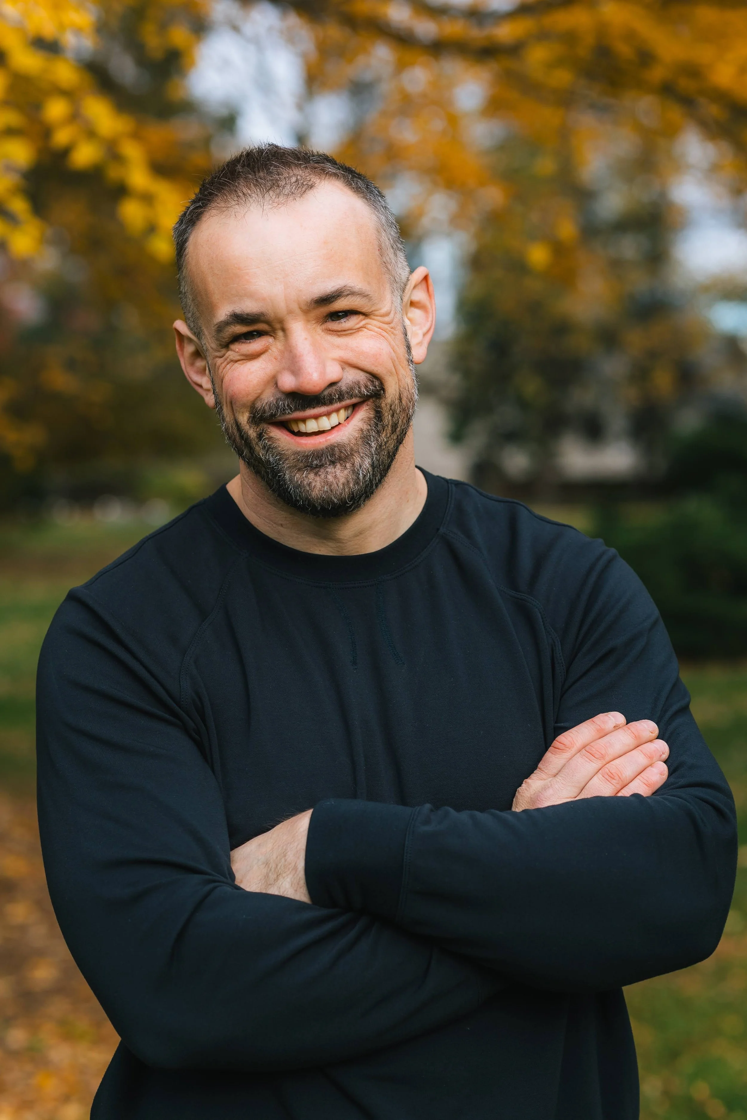 Jared Miller smiling outdoors with autumn trees behind him