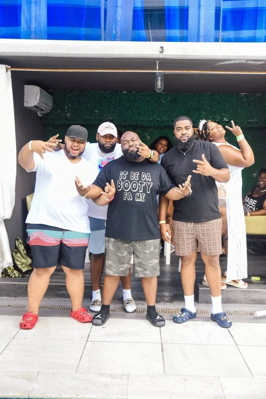 Group of six people posing together outside a building, making hand gestures and smiling.