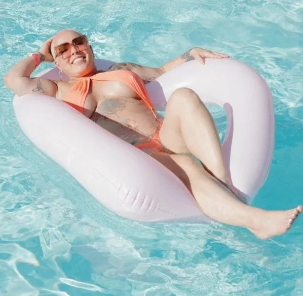 Woman relaxing on an inflatable pool float in the water, wearing sunglasses and a swimsuit.