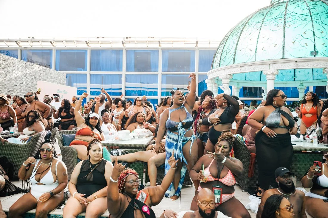 Group of women in swimsuits and summer outfits enjoying a rooftop pool party with a glass dome structure in the background.
