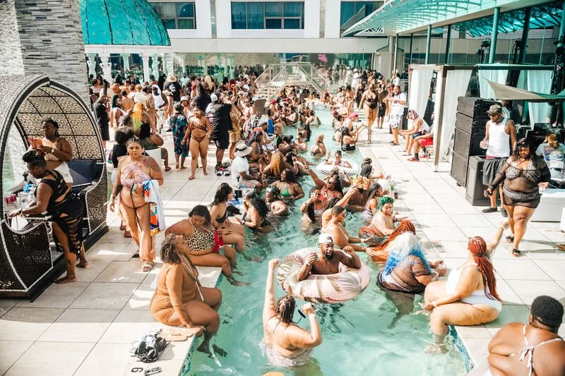 Crowd of people enjoying a pool party at a rooftop poolside area with many relaxing and socializing in the swimming pool and on the deck.