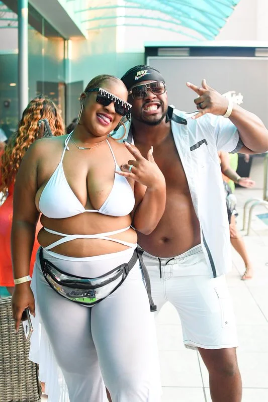 Two people, a woman and a man, are smiling and posing together outdoors, both dressed in summer attire.