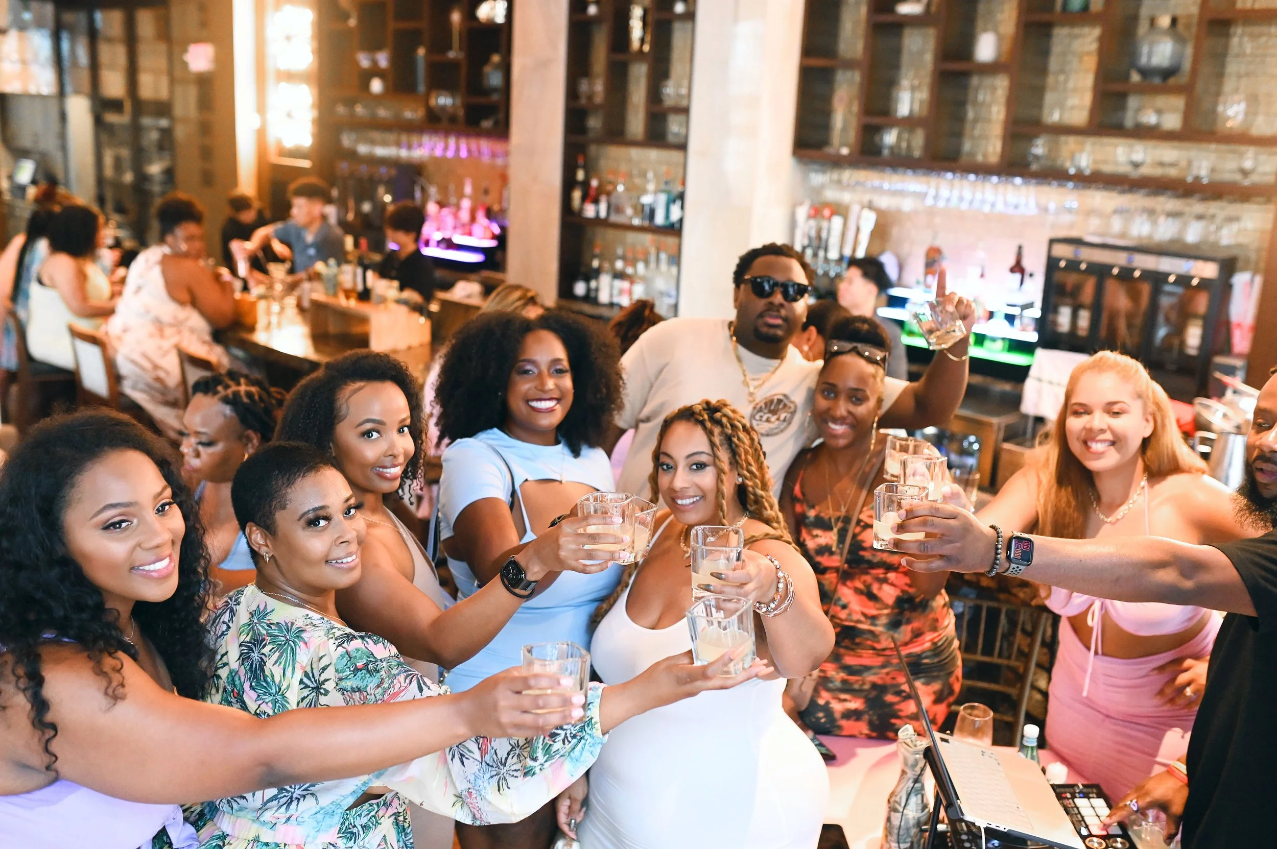 Group of friends celebrating with drinks at a bar, smiling and toasting.