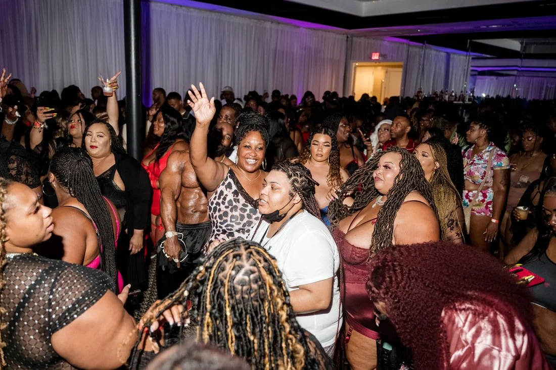 A lively crowded party with people dancing and enjoying themselves, including a woman smiling and waving at the center.