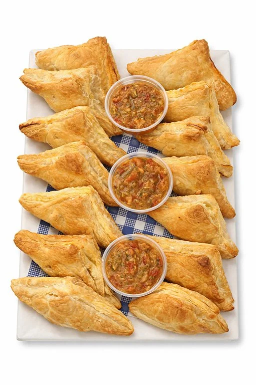 A white rectangular platter of pastries with three small cups of dipping sauce, arranged on a white surface.