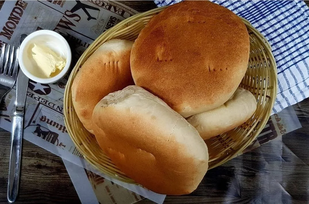Basket of chilean amasado bread rolls on a table with butter and utensils nearby.