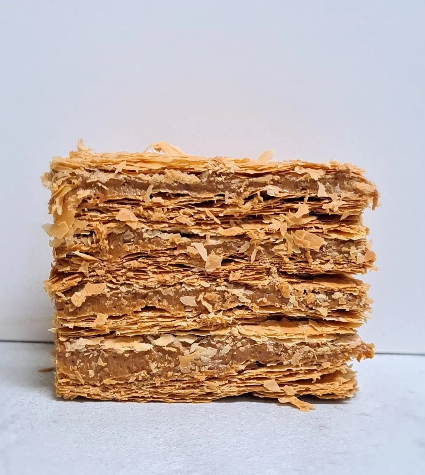 Close-up of a stack of layered, flaky, toasted pastry sheets on a white surface against a plain light background.