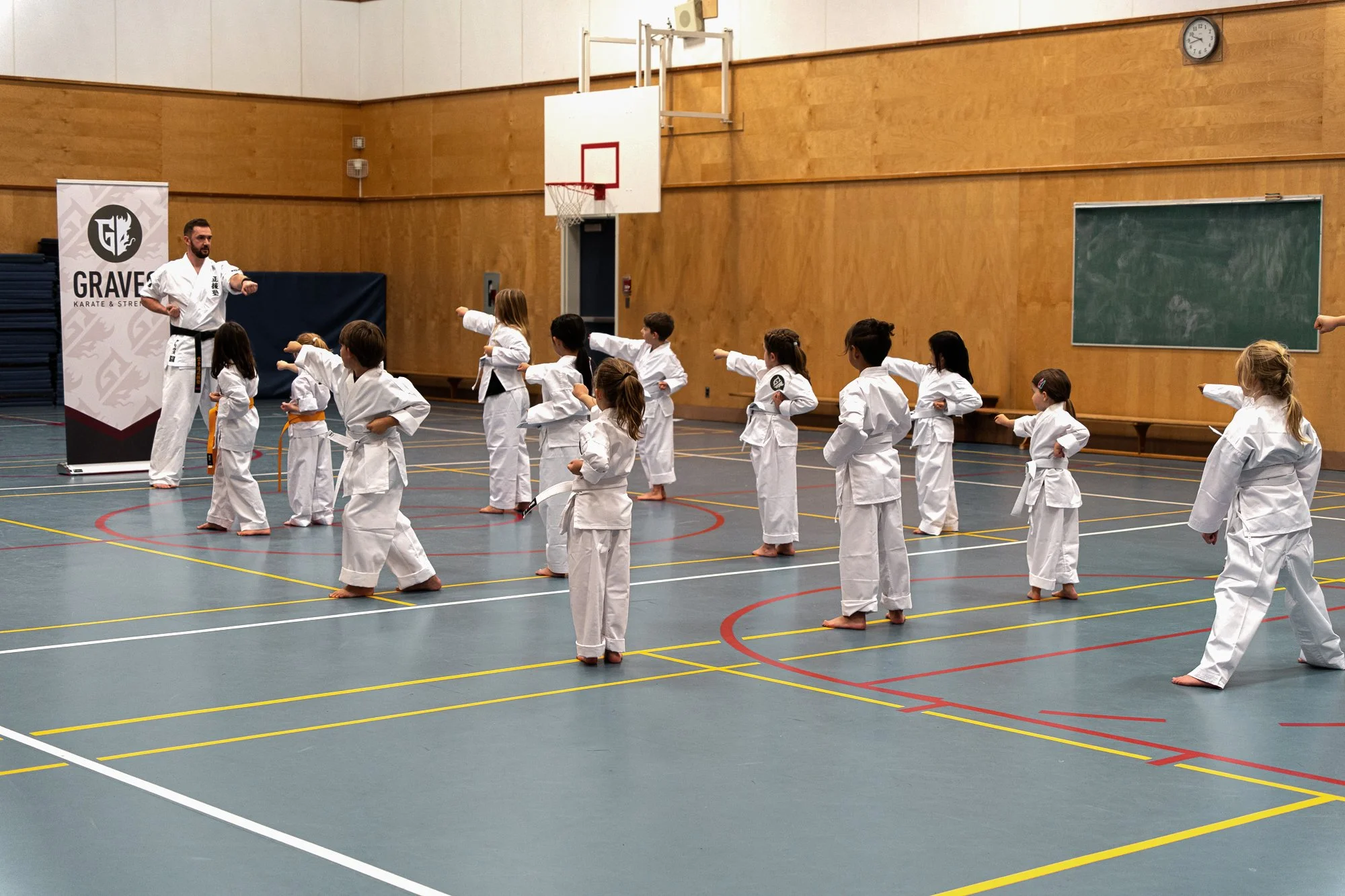 Martial arts instructor teaching a group of children in a gymnasium.