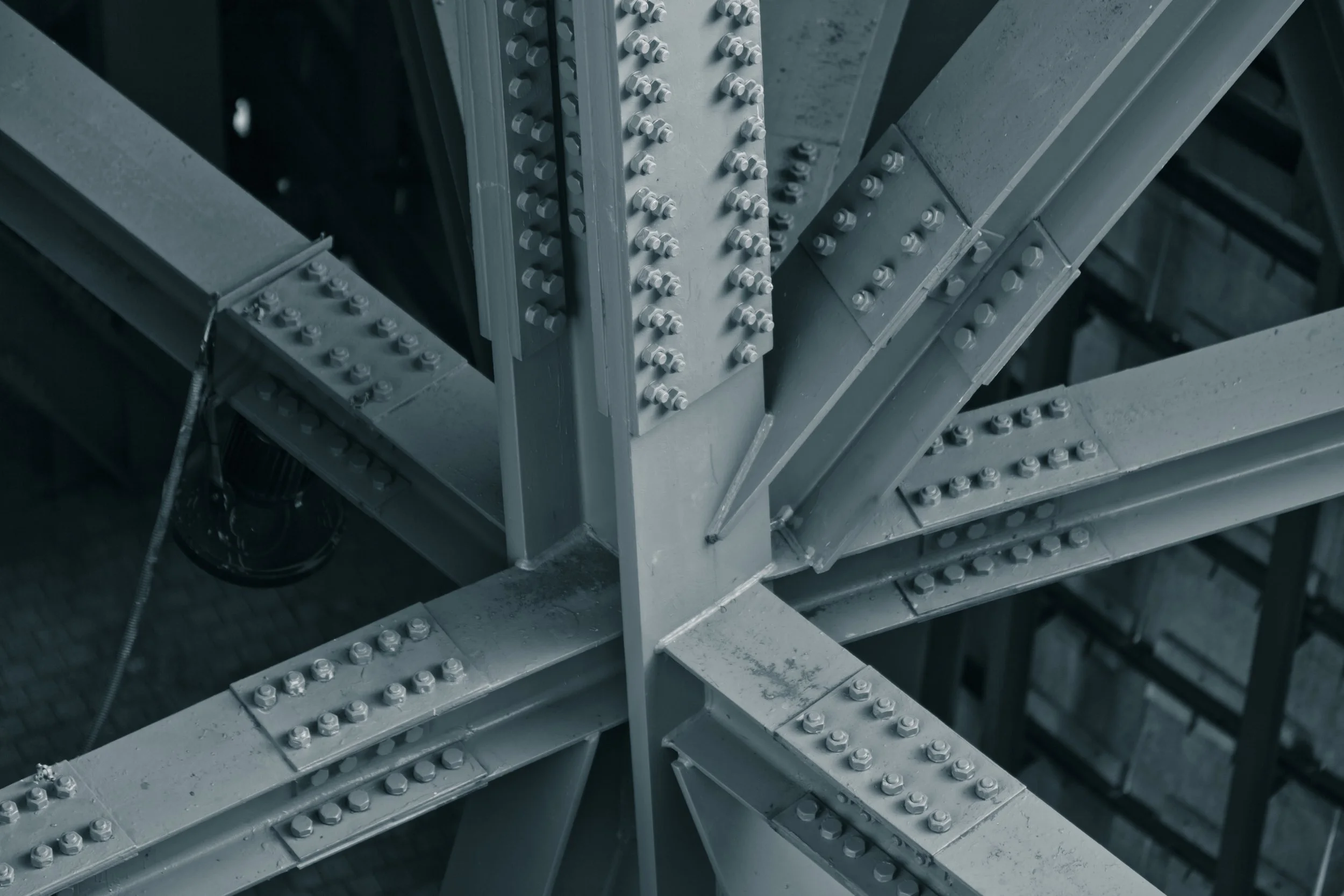 Vista desde abajo de la estructura de una torre metálica con varias vigas y tornillos de metal, formando una estructura sólida y resistente.