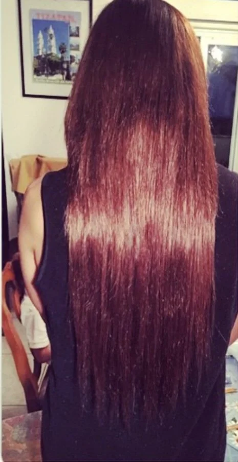 Back view of a woman with long, straight, and shiny reddish-brown hair standing in a room.