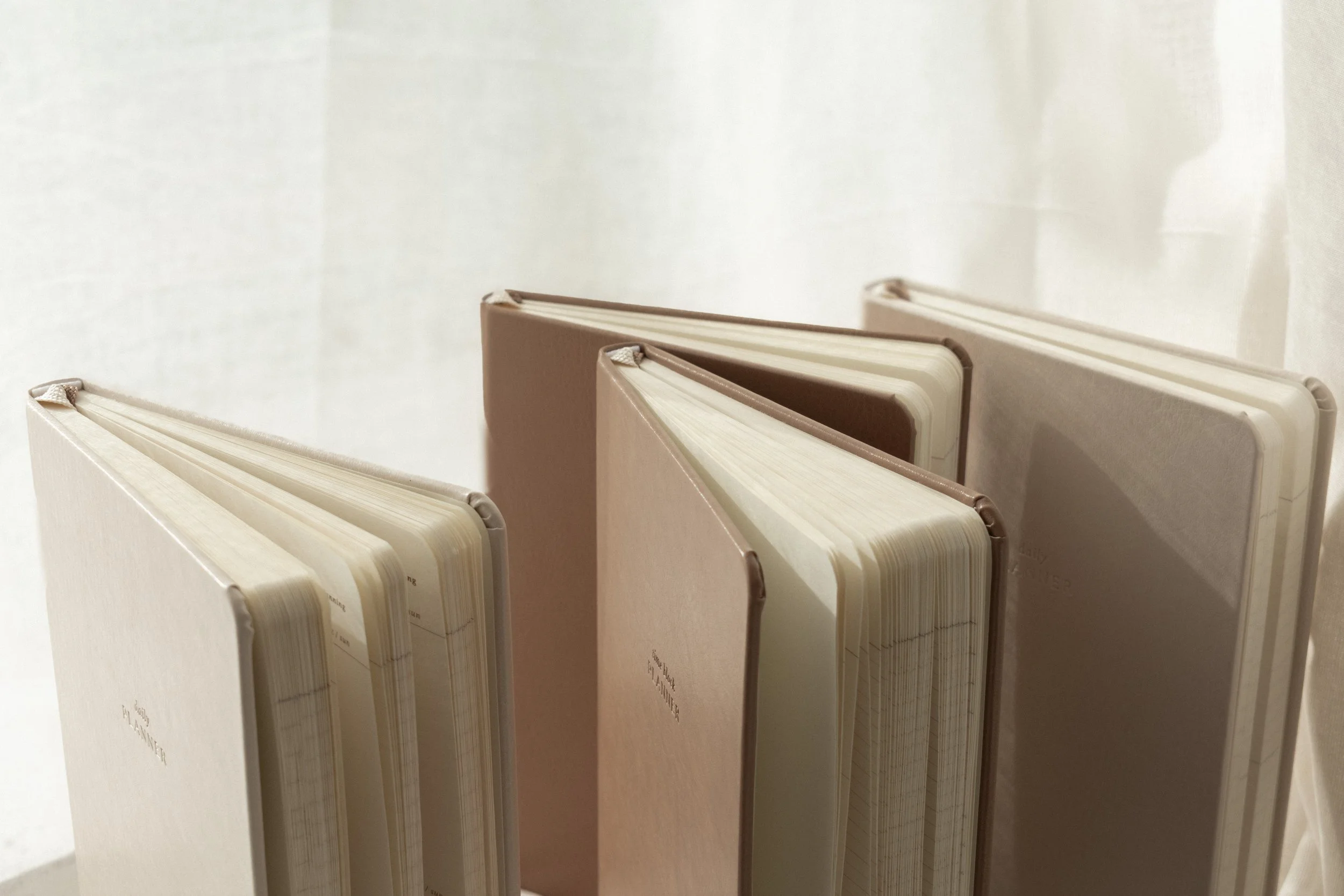 Four beige and white notebooks standing upright on a light-colored surface.