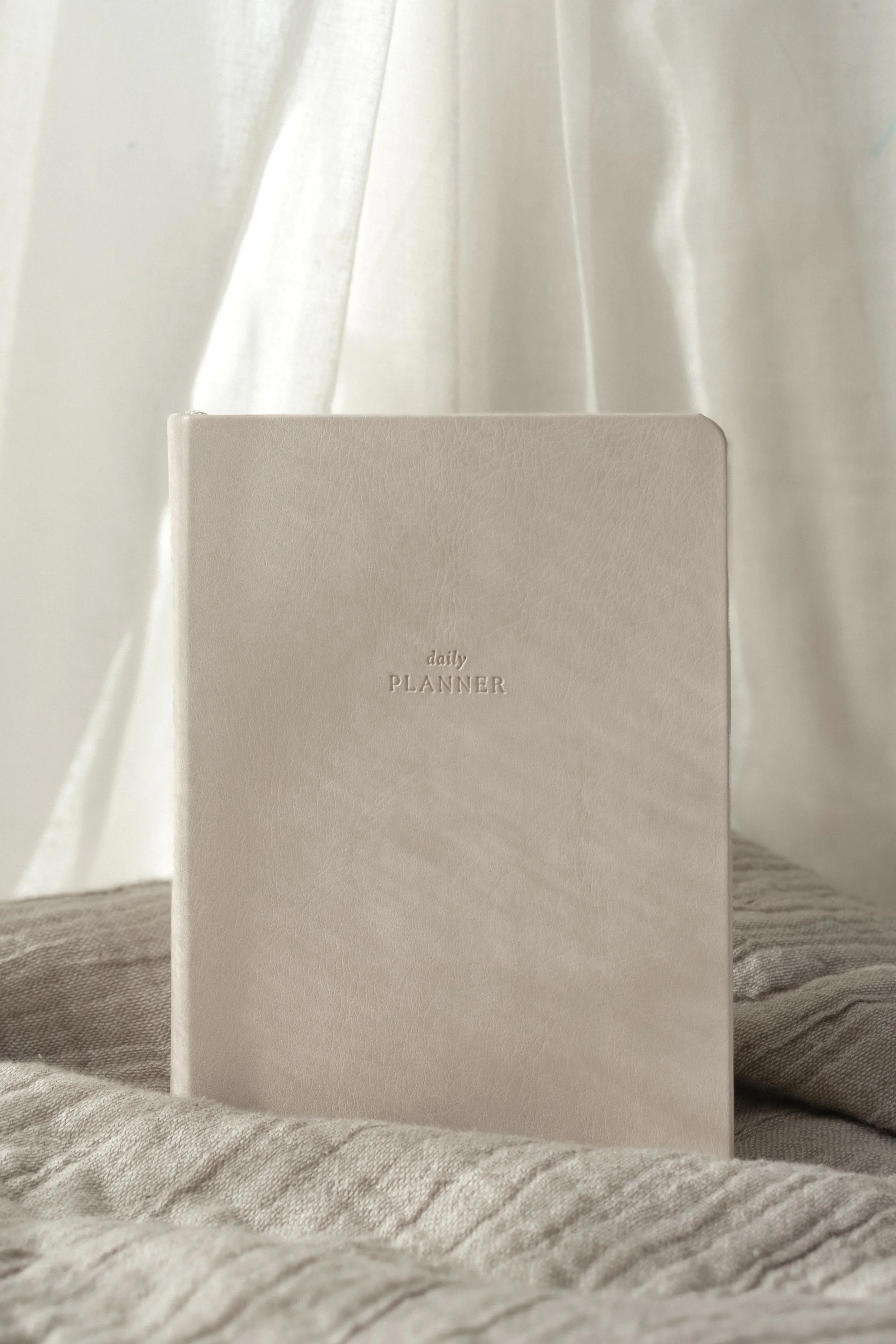 Linen color undated daily planner, soft fabric backdrop and light cascading over the planner