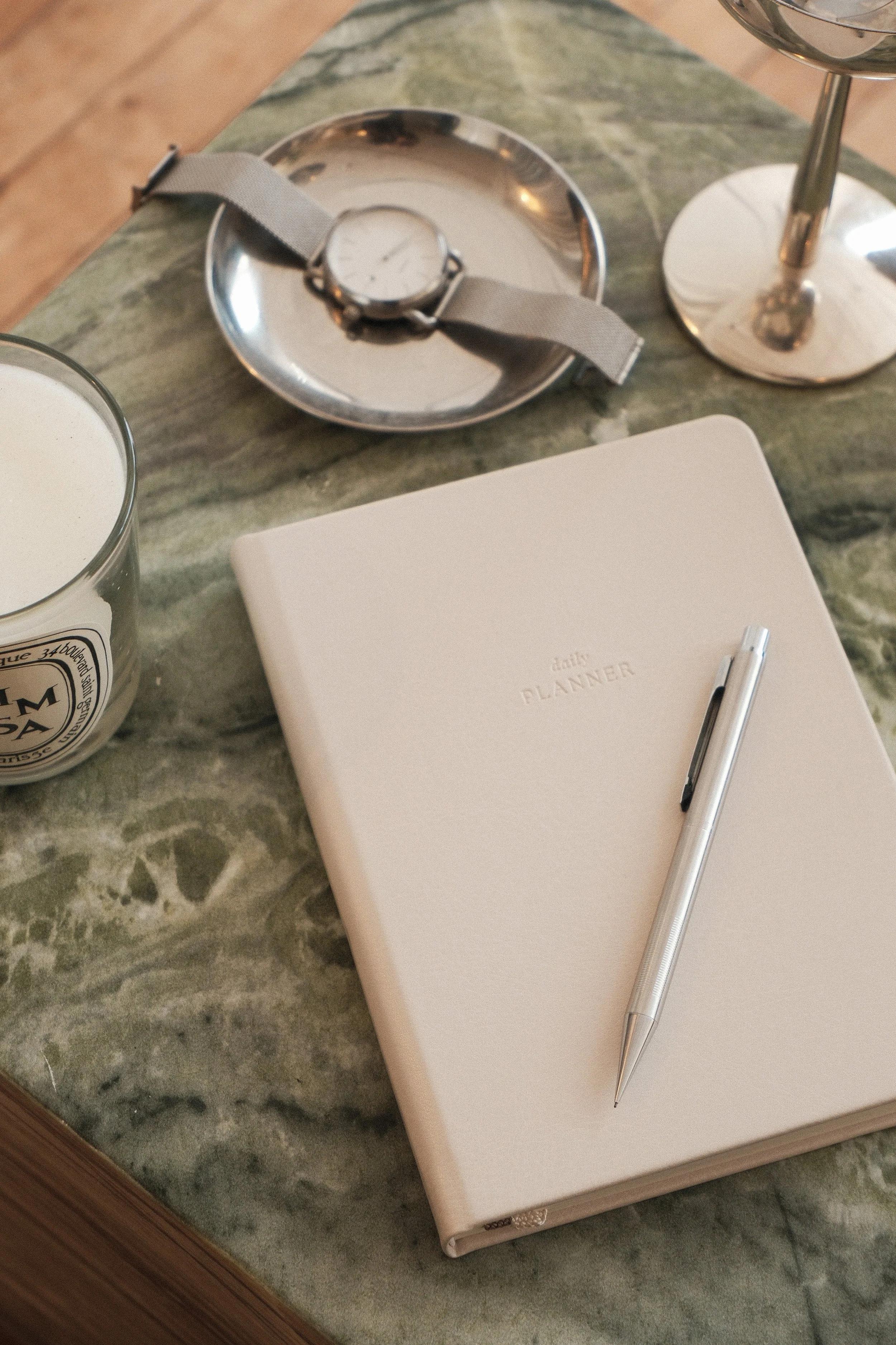 Off-white vegan leather daily planner on a green marble side table