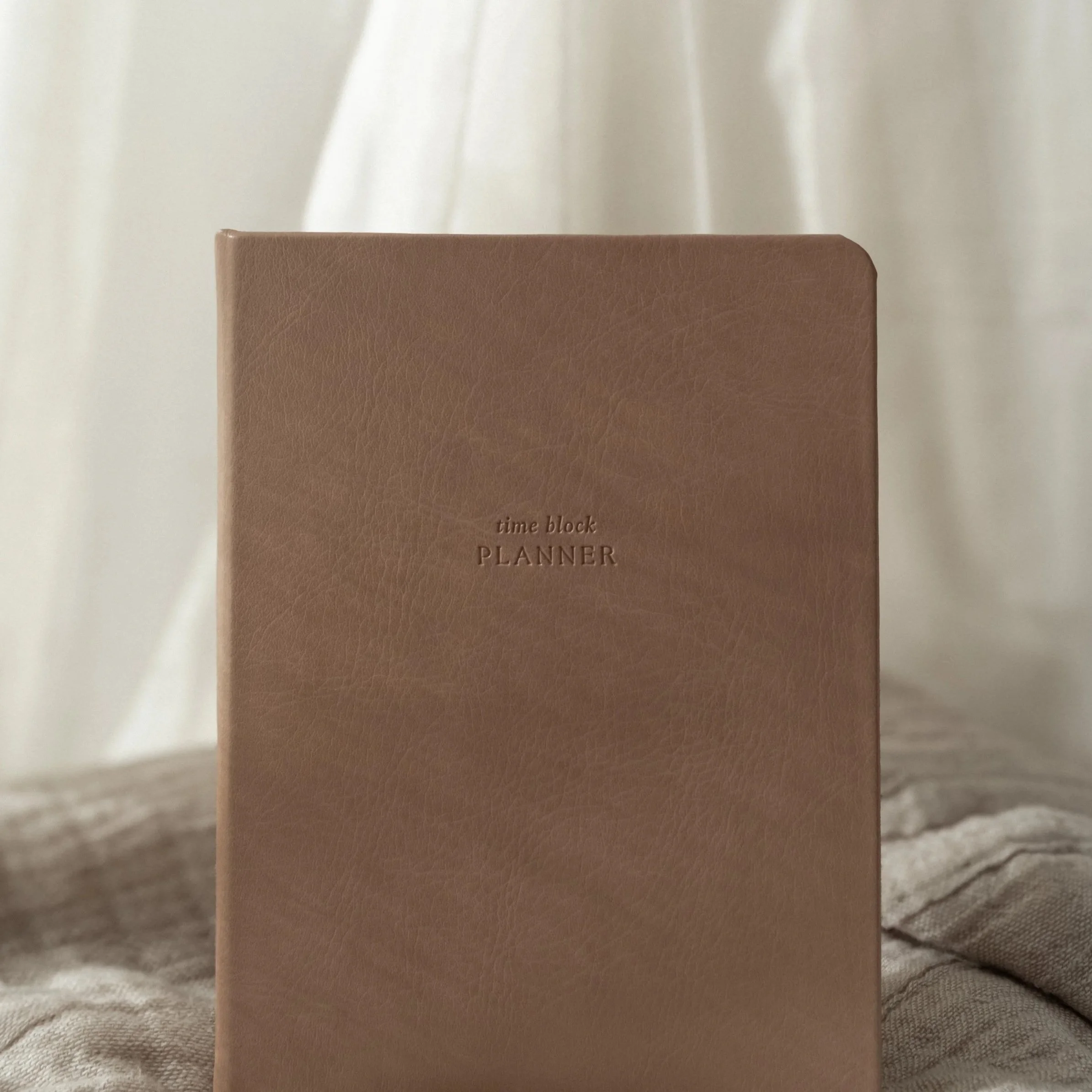 A closed brown planner with the words "time block PLANNER" embossed on the cover, placed on a soft surface with a light background.