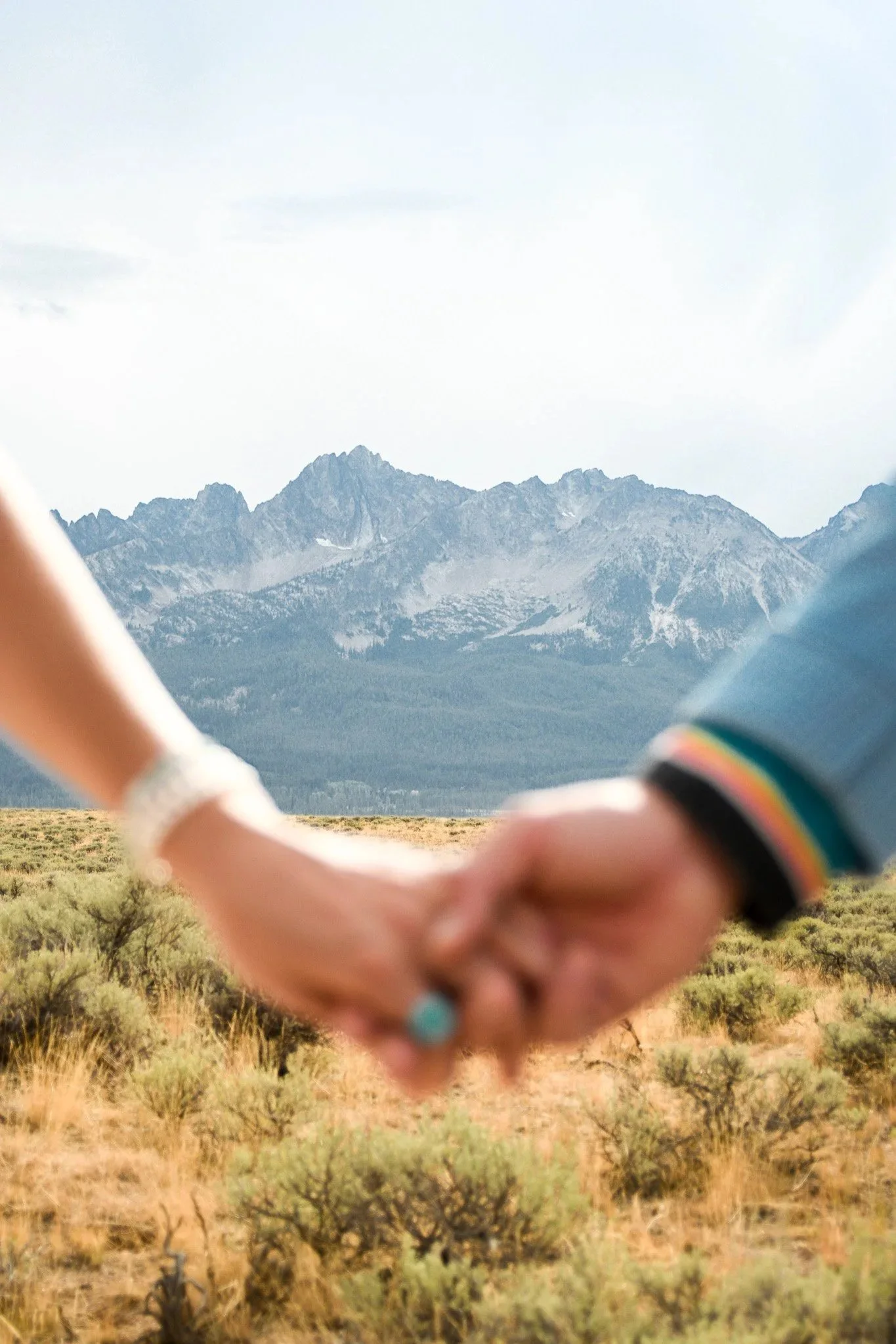Close-up of a couple holding hands in a desert landscape with mountains in the background.