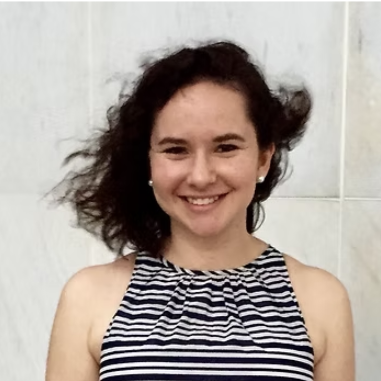 A young woman with shoulder-length curly brown hair, smiling, wearing pearl earrings and a sleeveless, striped top.