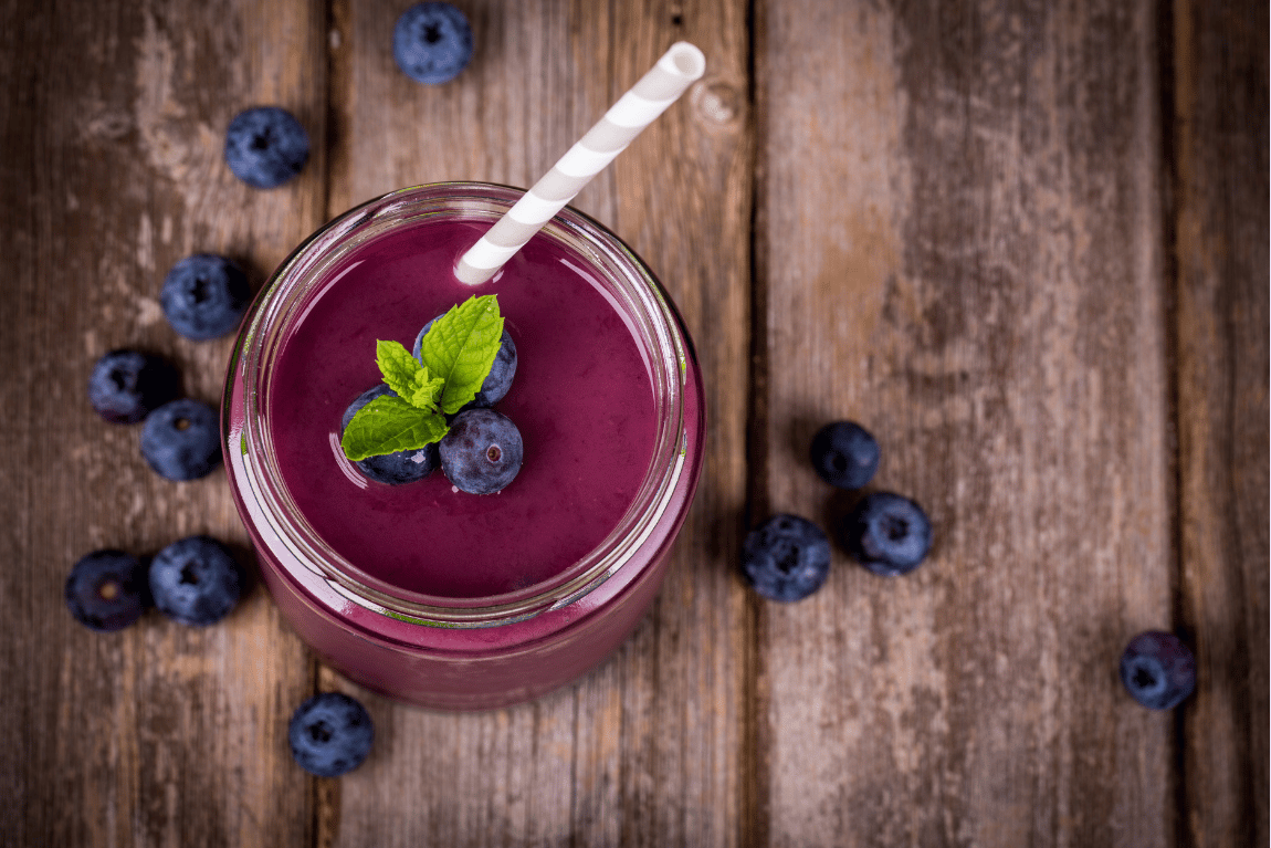 Rebirth Superfood Mushroom Blend For daily wellness, A blueberry smoothie in a jar with a striped straw, garnished with blueberries and a mint leaf, on a wooden surface surrounded by more blueberries.