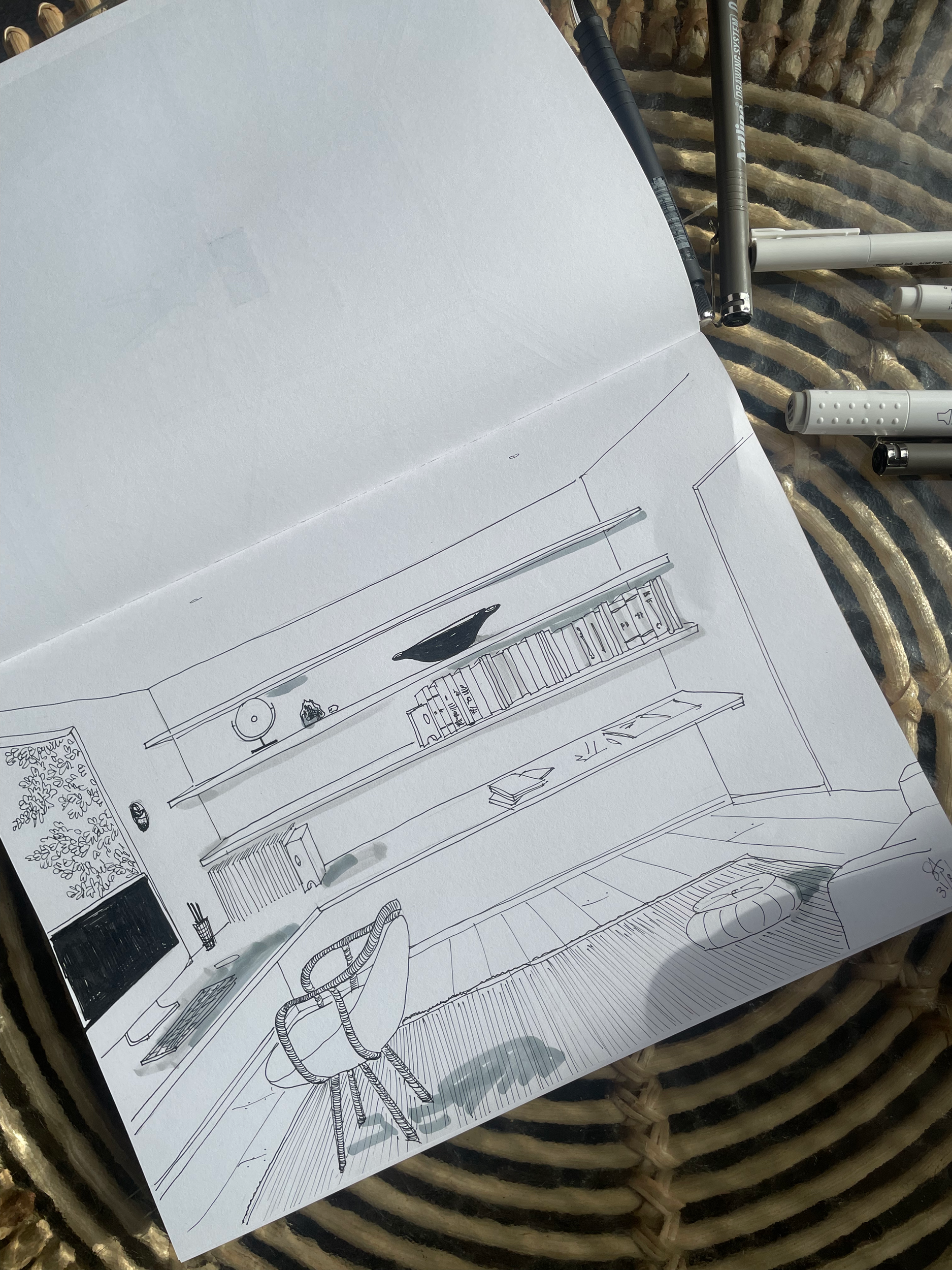 A black and white sketch of a living room with a bookshelf, a TV, and a chair, along with some drawing tools on a table.