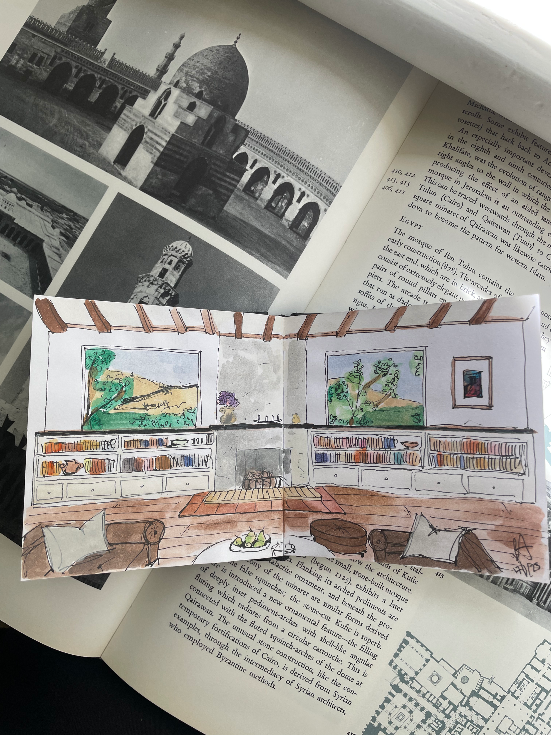 A hand-drawn interior scene of a living room with two windows, a fireplace, bookshelves, a sofa, an armchair, and decorative pillows.