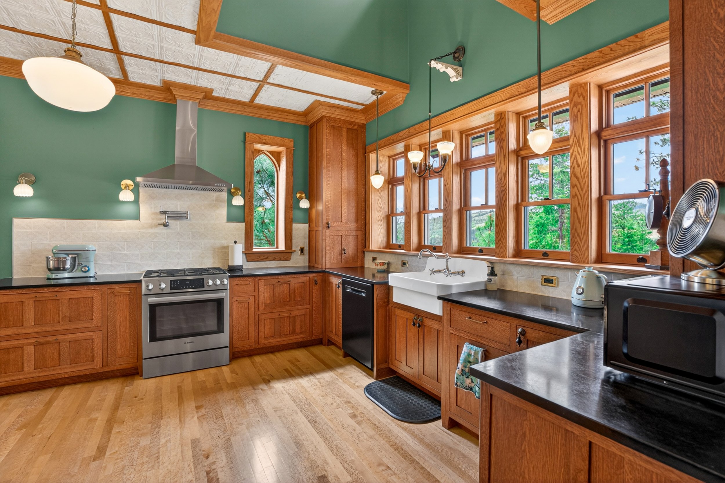 Chewelah Real Estate Photography - Kitchen with green walls, wooden cabinets, large windows with views of trees.