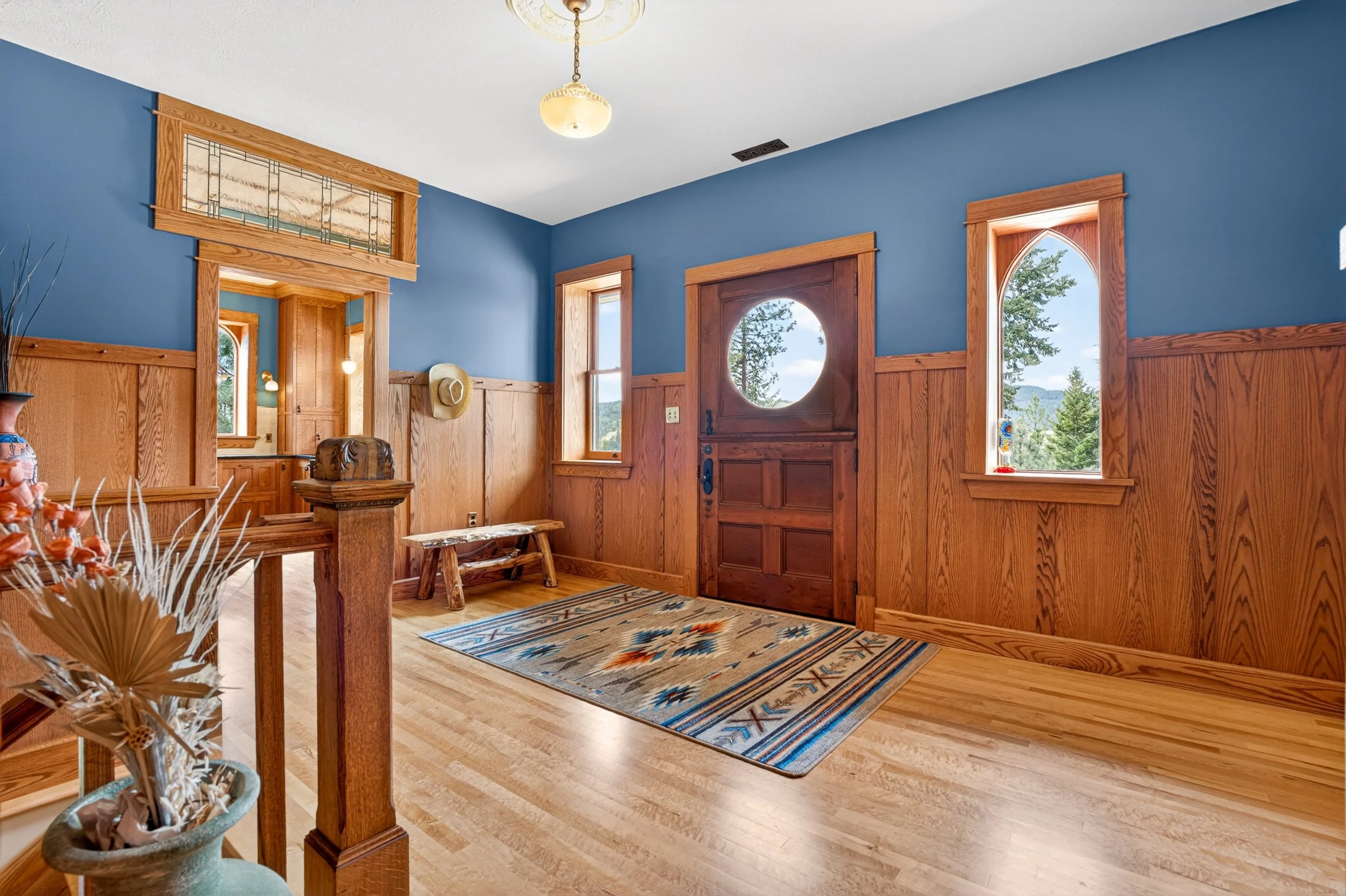 Chewelah Real Estate Photography - Interior view of a house entryway with blue walls, wooden trim, and a wooden door with a circular window. 