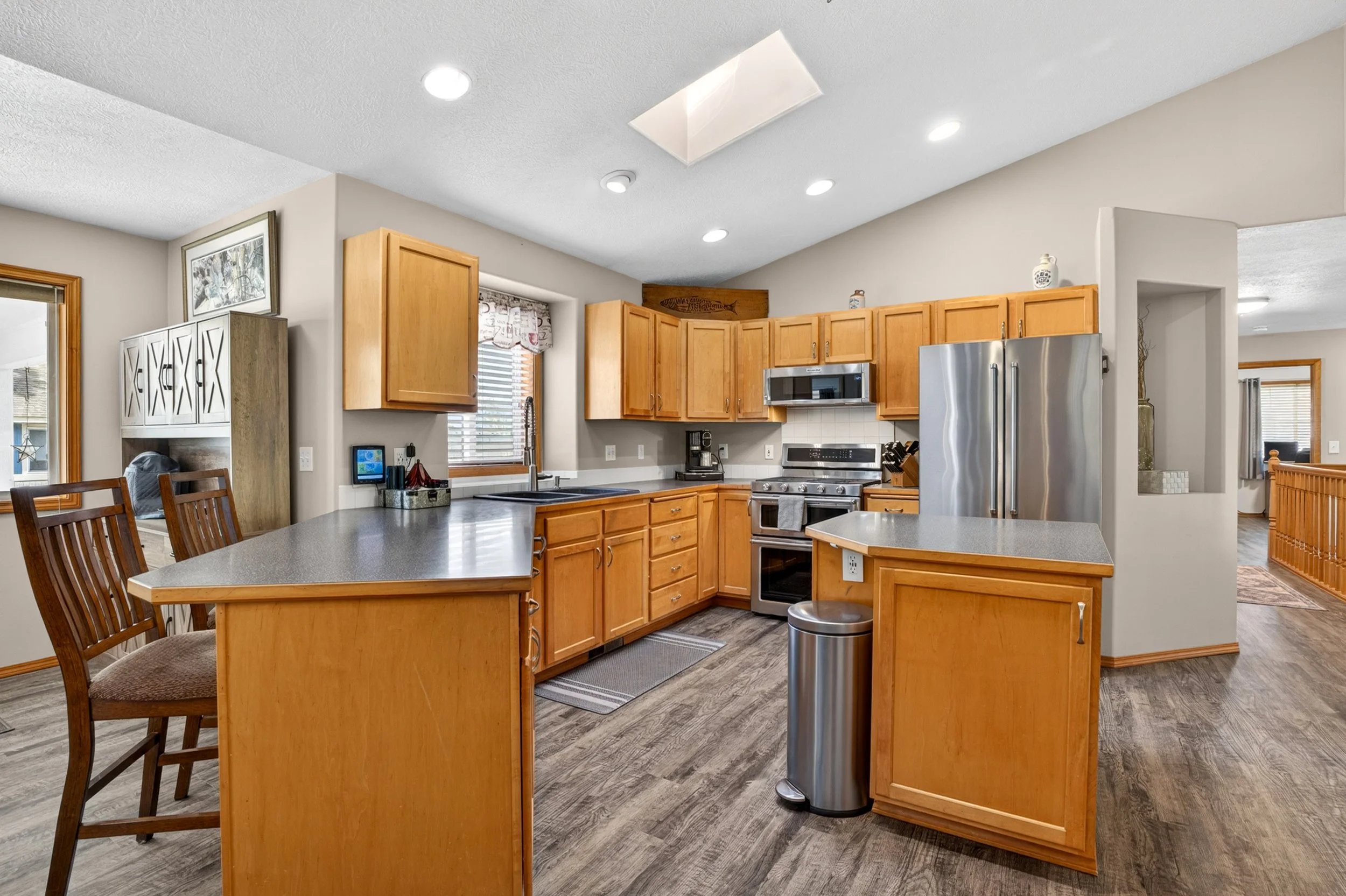 Spokane Real Estate Photography - Kitchen with wooden cabinets, stainless steel refrigerator, microwave, and a breakfast bar with wooden chairs