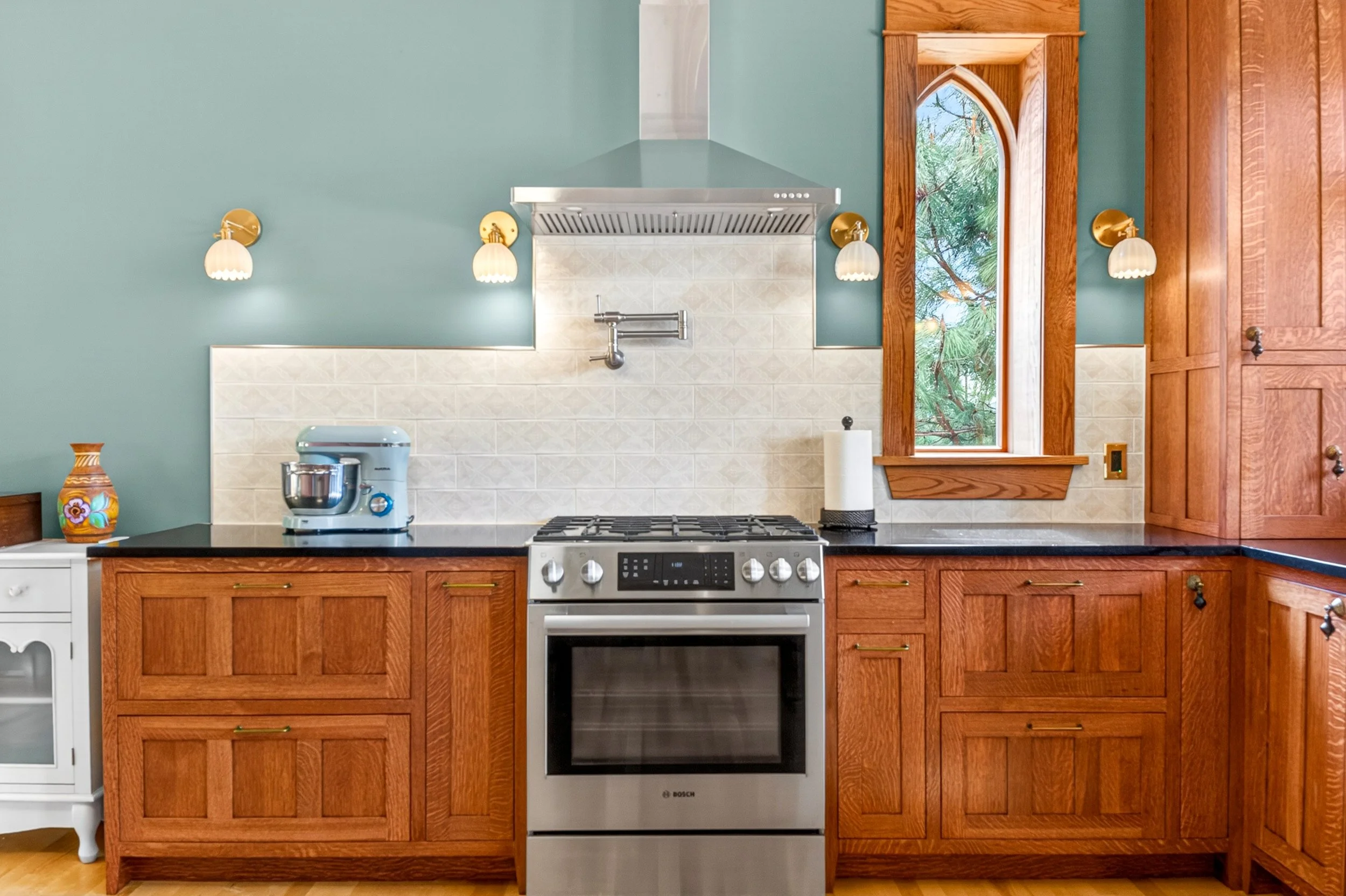 Chewelah Real Estate Photography - Kitchen with wooden cabinets, stainless steel oven, blue walls, and a window with a view of trees.