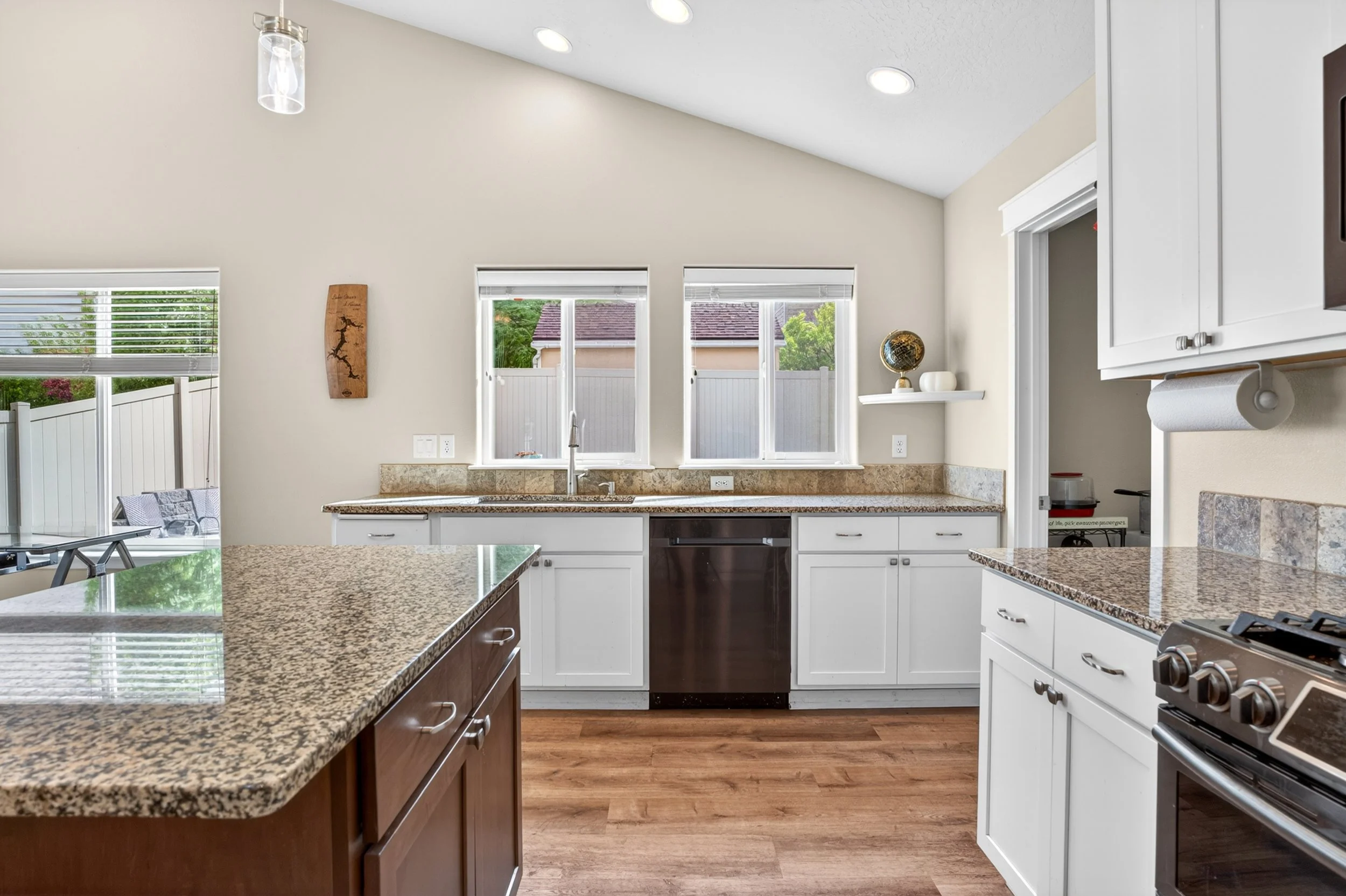 Spokane Real Estate Photography - Modern kitchen with white cabinets, granite countertops, and wooden flooring, featuring three windows, a sink, and various kitchen appliances.