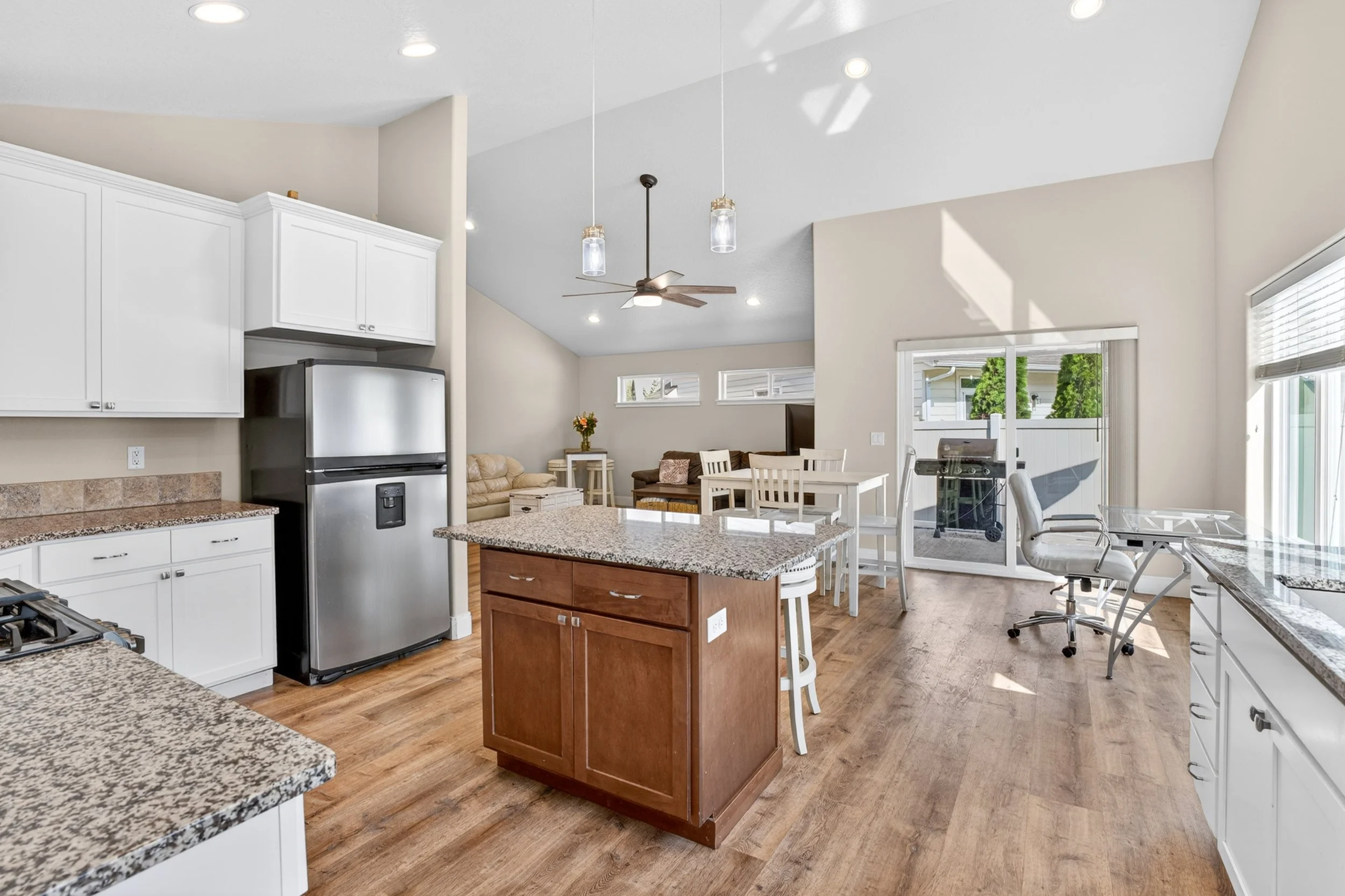 Spokane Real Estate Photography - Open-concept kitchen and living room with white cabinets, granite countertops, and a kitchen island with a wooden base. Recessed lighting, pendant lights, and a ceiling fan are visible.