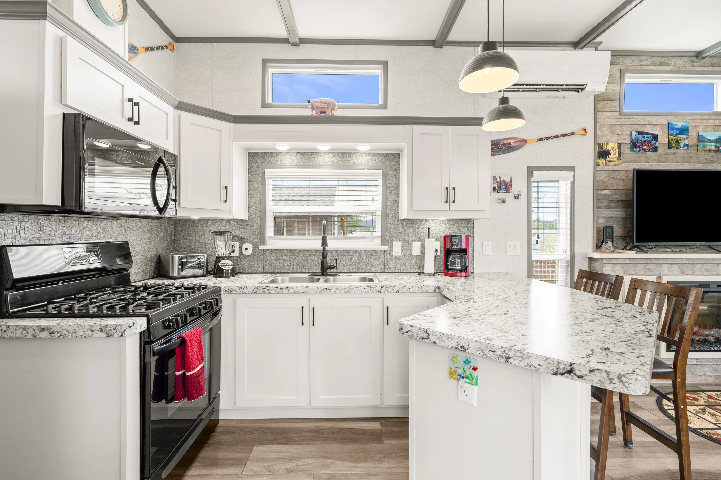 Pend Oreille County Real Estate Photography - A modern kitchen with white cabinets, a marble countertop, stainless steel appliances, and a window above the sink.