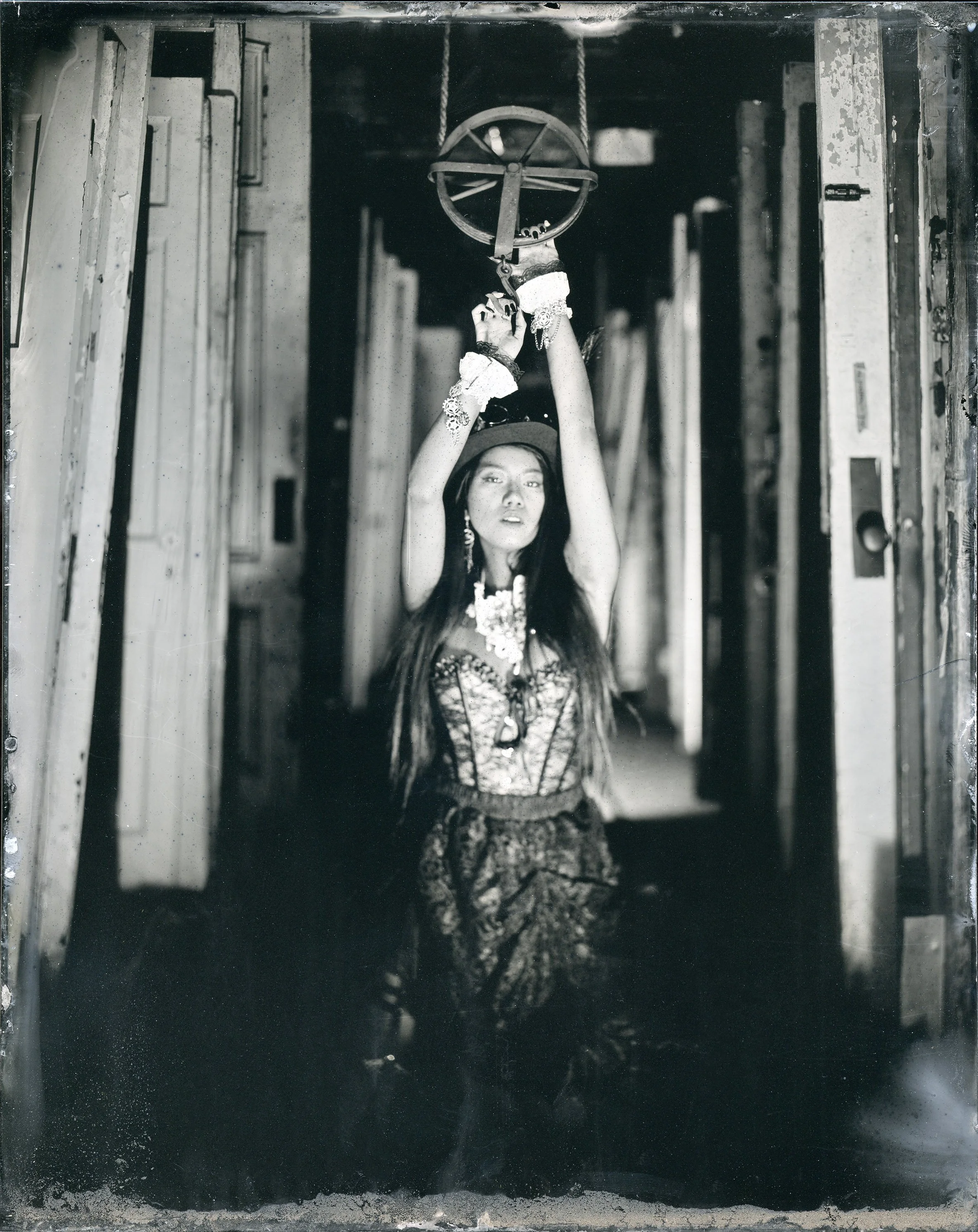 A woman in traditional attire holding a spinning wheel above her head in an industrial or workshop setting.