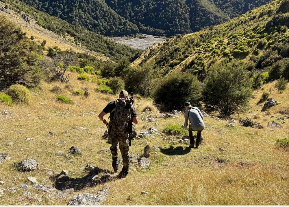A guide and hunter crossing tussock slopes above a river
