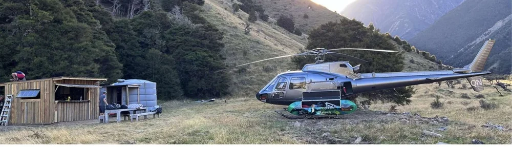A helicopter parked beside a backcountry hut at the edge of the forest