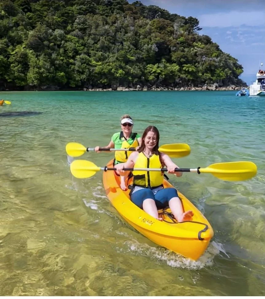 Two guests paddling a yellow double kayak in clear shallow water