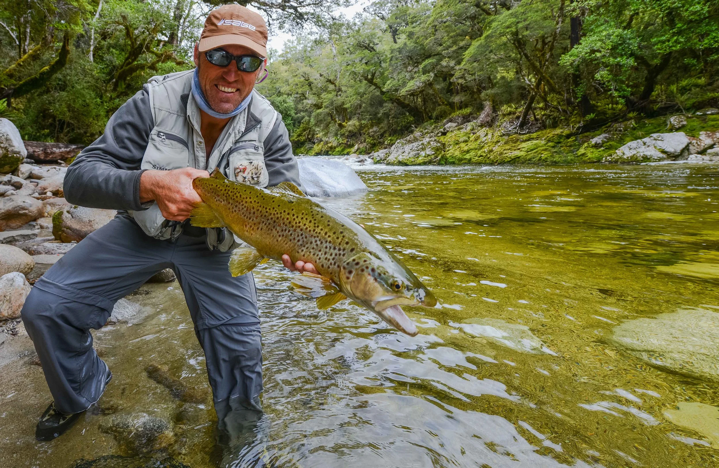 Fly fisherman showing off a trophy brown trout in the river near Stonefly Lodge