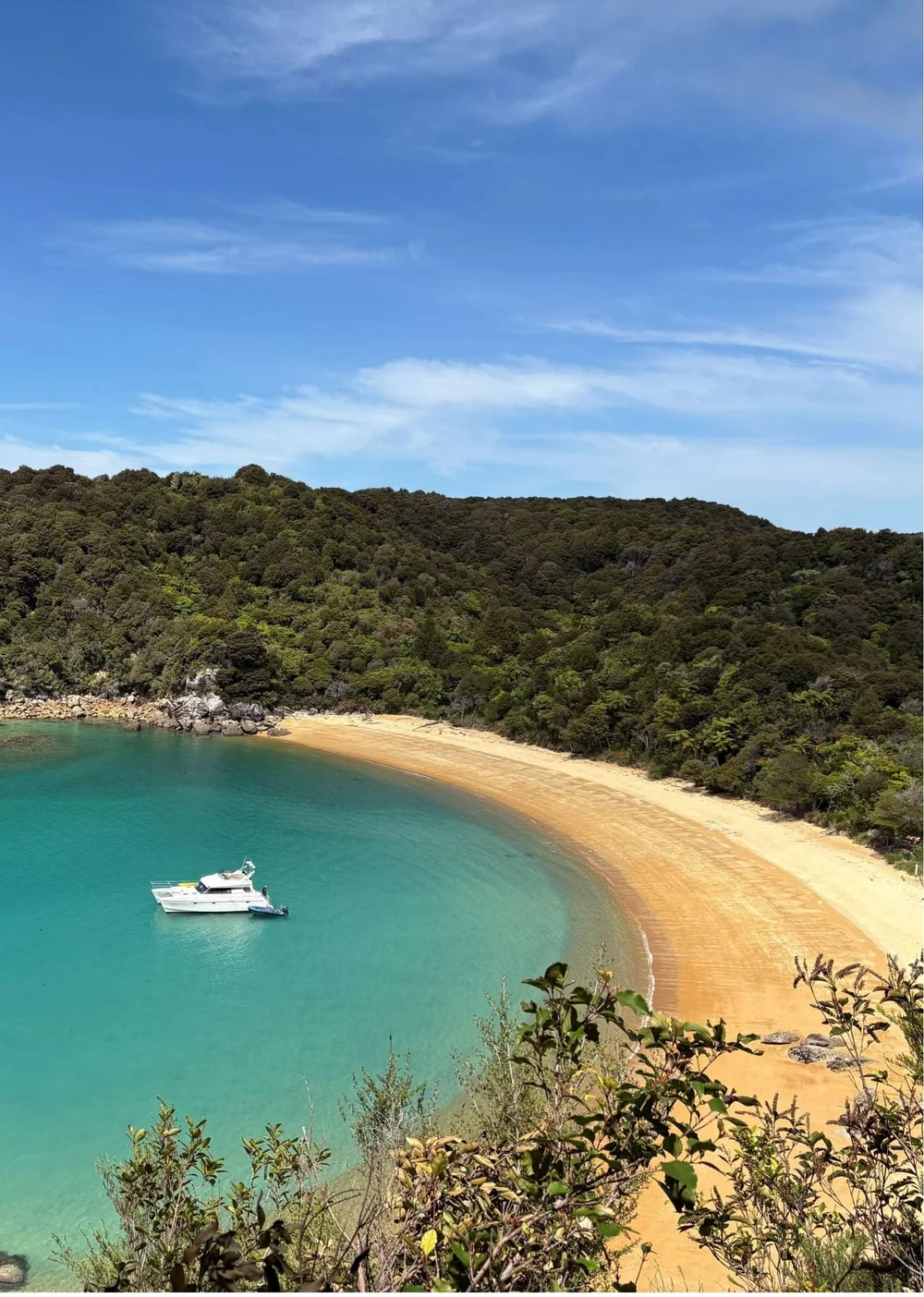 A white launch moored in a turquoise bay below a curve of golden sand