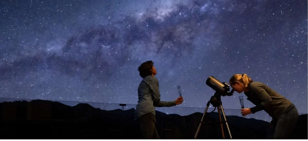 Two guests under the Milky Way, one looking through a telescope