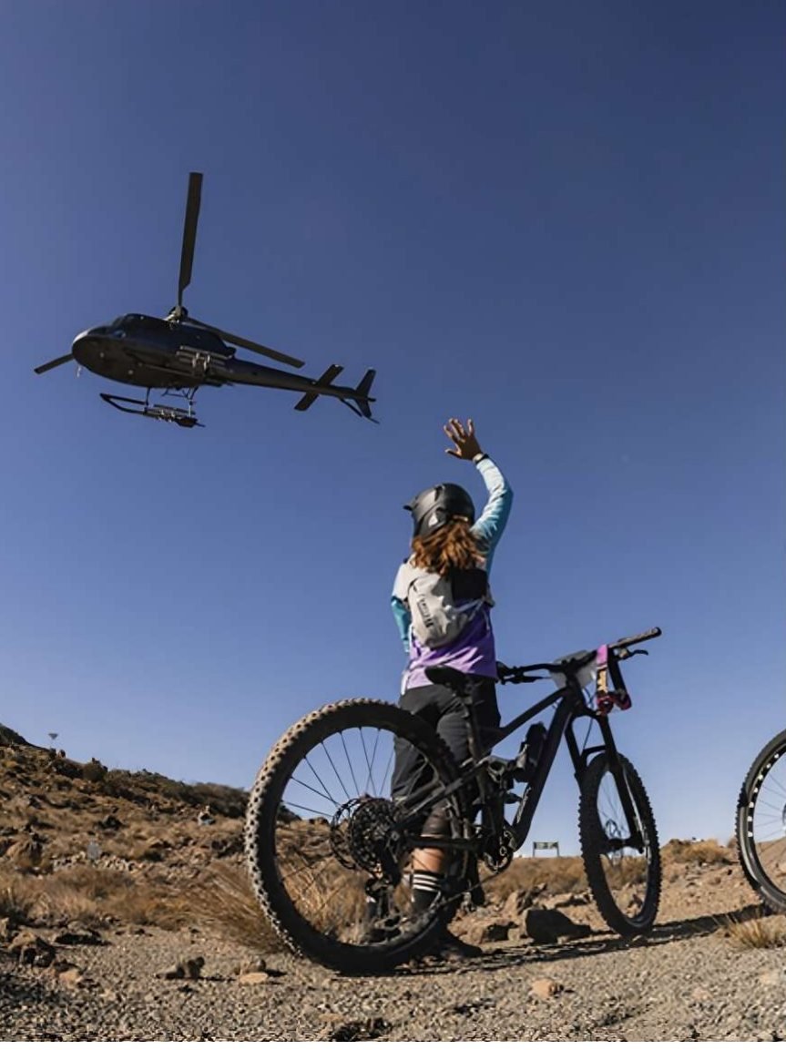 A rider waving to a helicopter overhead on an exposed ridge