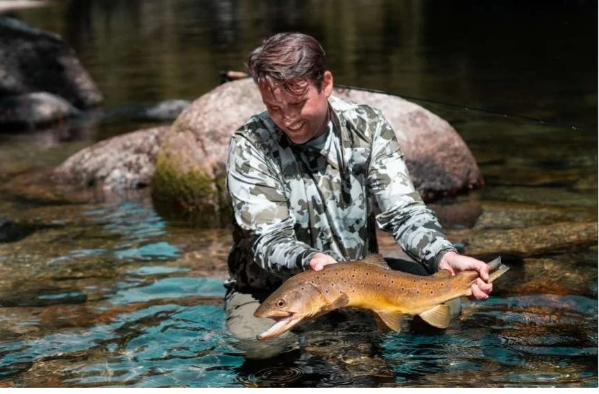 An angler crouched in the shallows releasing a brown trout