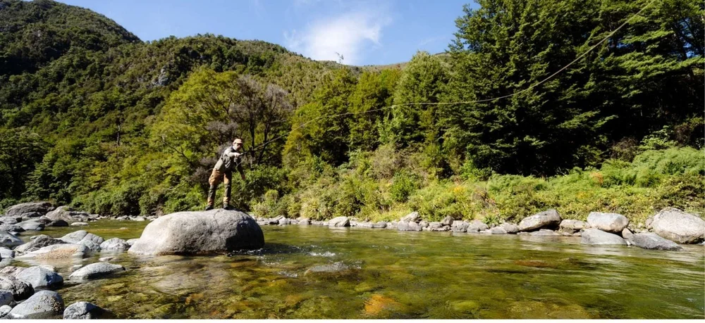 An angler casting from a boulder in the Motueka River