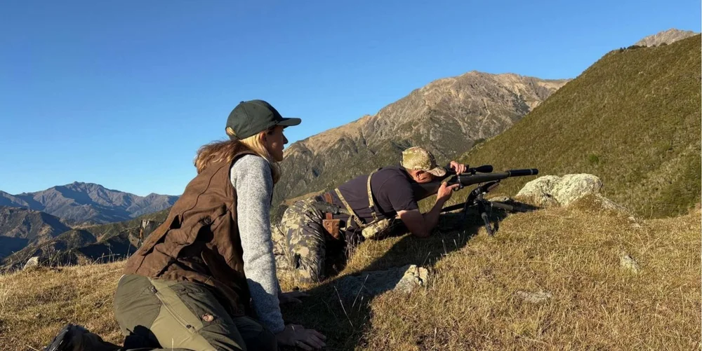 Two hunters glassing a mountain slope from a grassy ridge