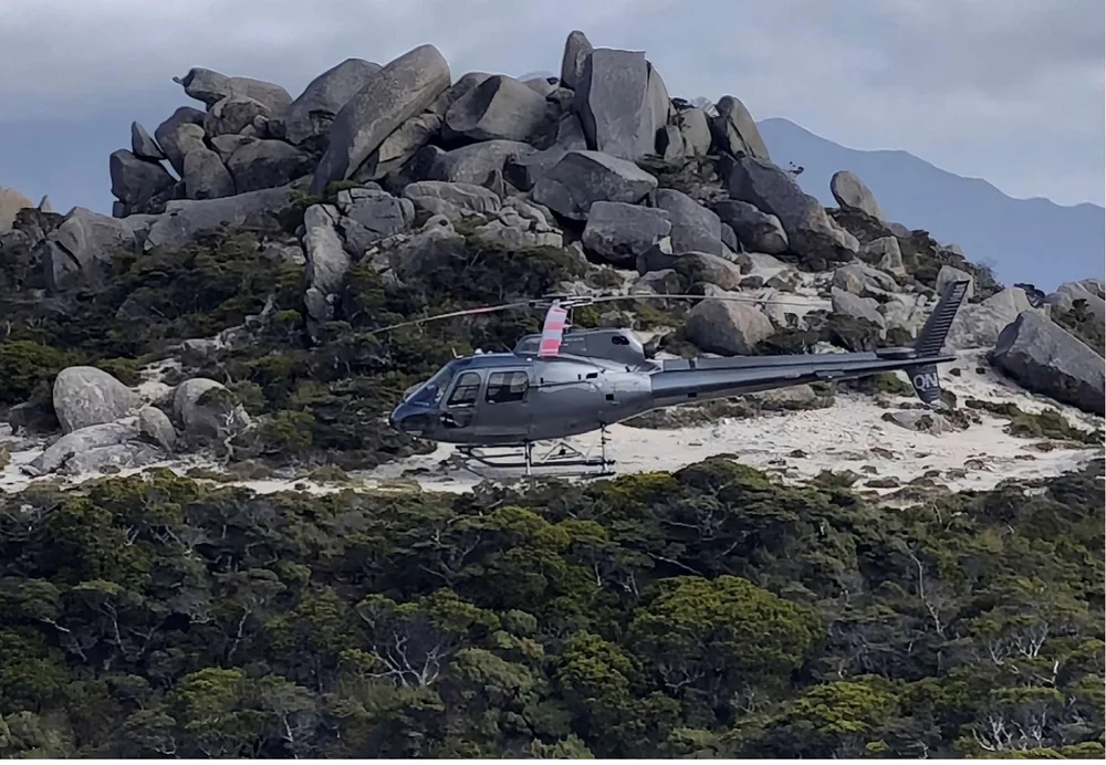 A helicopter landed among giant boulders on Mt Owen