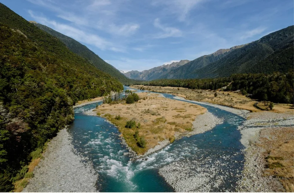 A turquoise backcountry river winding between beech forest and tussock flats