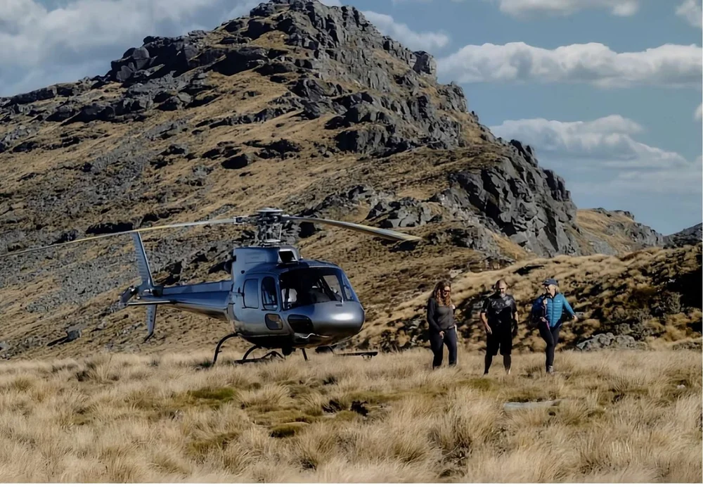 A helicopter landed in tussock country with three guests walking towards it